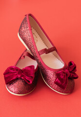 Shiny red ballerinas with velvet bows on red background