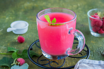 Traditional Russian hot drink raspberry jelly or kissel in a glass transparent mug on a green concrete background.