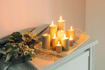 Tray with burning candles and beautiful flowers on chest of drawers in room