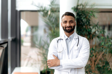 Portrait of an Indian general medicine doctor, stands with arms crossed in a clinic, dressed in...