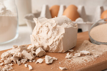 Wooden board with fresh and dry yeast on light background