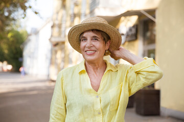 happy senior woman in sun hat walks  on summer city