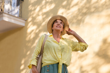 happy senior woman in sun hat walks  on summer city