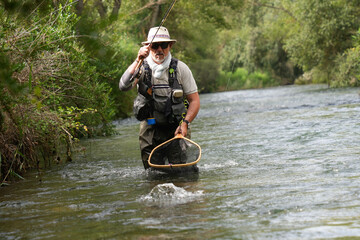 fly fisherman catching a big wild fish in a small river