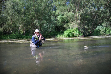 fly fisherman catching a wild trout in a small river