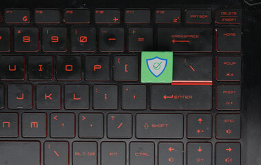 Laptop keyboard with green wooden block and shield sign. Anti-virus updated.