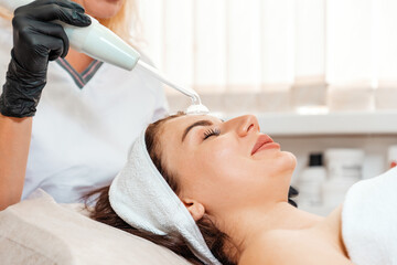 Darsonval cosmetology apparatus. Beautician cleans the client's forehead using a electric device. Concept of professional procedure in salon