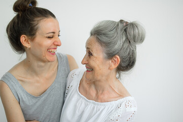Happy senior mother is hugging her adult daughter, the women are laughing together, sincere family of different age generations having fun on white background, mothers day.