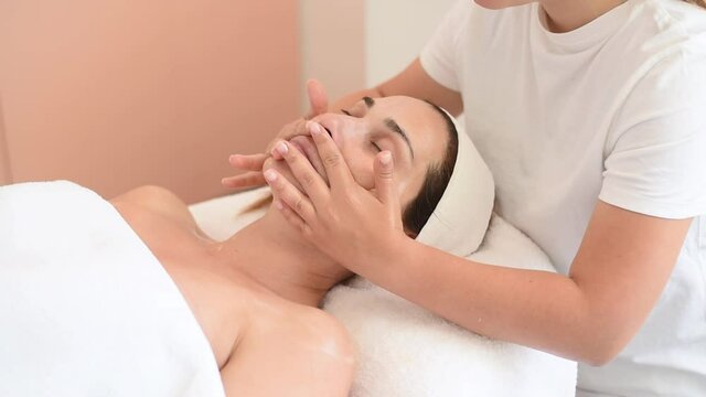 Cosmetologist make massage on face. White clothes. For beautiful woman do healthy procedure, moisturise receiving nutritious facial peeling. Beauty treatment skin care in cosmetology spa salon