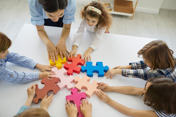 Female teacher engaging kids in teamwork. Little children participate in fun group activity in...