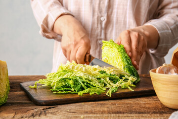 Woman cutting fresh savoy cabbage at table