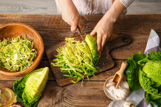 Woman cutting fresh savoy cabbage on wooden background