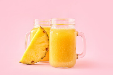 Mason jars of tasty pineapple smoothie on color background