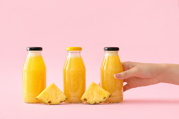 Female hand with bottles of tasty pineapple smoothie on color background