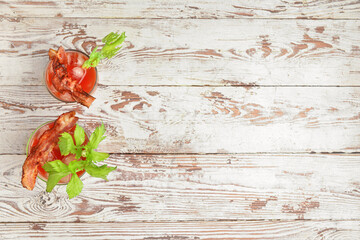 Glasses of bloody mary cocktail garnished with bacon and cilantro on light wooden background