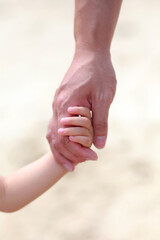 Close up of father holding his daughter hand while walking on the beach.