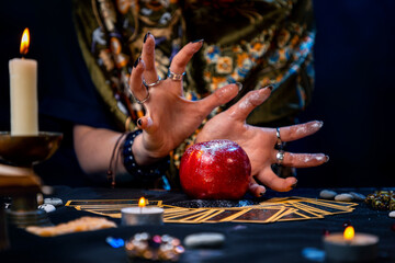 A fortune teller conjures a red apple lying on the Tarot cards. On the table is a lighted candle and amulets. Close up. The concept of divination, astrology and esotericism