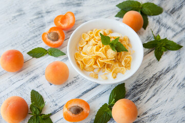 Corn Flakes with apricot at the white wooden table. Healthy summer breakfast which consist of different yellow ingredients. breackfast corn flakes with apricot