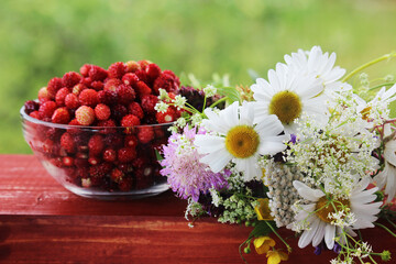 Fototapeta na wymiar A glass bowl with strawberry and a daisy bouquet