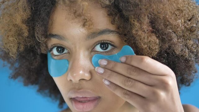 Professional African American model with short curly hair applies blue patches on face under eyes standing in studio close view