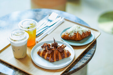 Croissants on dishes with iced coffee and iced lemon tea put on a marble table served at café in afternoon light , selective focus