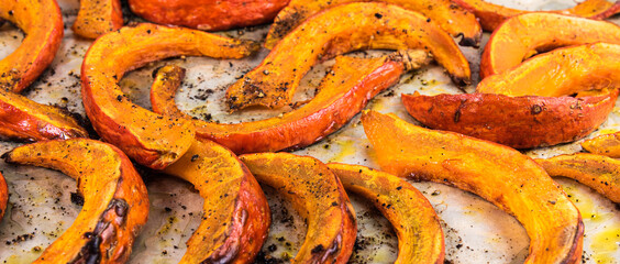 Baked pumpkin slices cut into slices on parchment - close-up, panoramic view