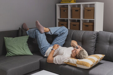 A woman lies on a sofa with a smartphone in a minimalistic home interior. High quality photo