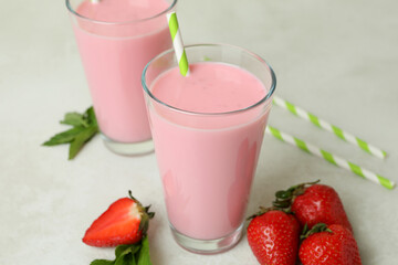 Glasses of strawberry milkshake and ingredients on white textured tableGlasses of strawberry milkshake and ingredients on white textured table