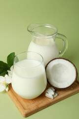 Milk, flowers and coconut on board on green background