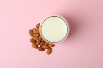 Glass of milk and almonds on pink background