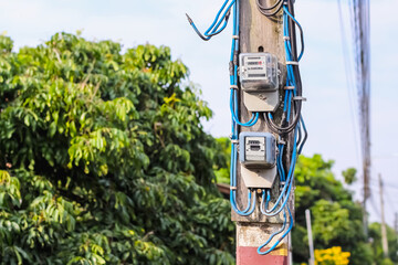Close up electric meters on pole in front of home with blue sky and tree background rural landscape of Thailand