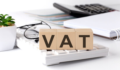 VAT written on a wooden cube on keyboard with office tools - obrazy, fototapety, plakaty