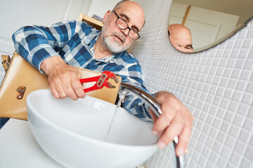 Installateur mit Rohrzange repariert Armatur im Bad