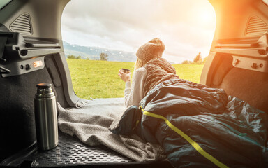 Girl resting in her car. Woman hiker, hiking backpacker traveler camper in sleeping bag, drinking...