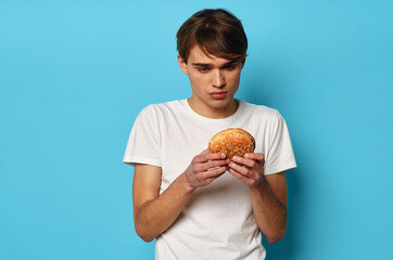 a man in a white t-shirt with a hamburger in his hands lunch blue background