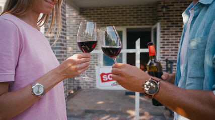 cropped view of couple clinking glasses of red wine near new house.