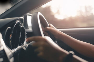 Hand holding on black steering wheel while driving in the car, a driver traveling on a road to the...