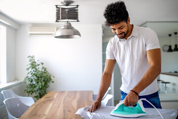 Happy young handsome black man ironing clothes at home