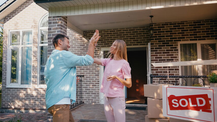 happy couple giving high five near new house and sold board.