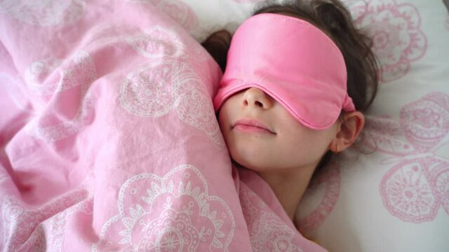 Sleeping little girl in sleep  in bed  late in morning. Pretty child sleeping in her bed with pink eye sleeping mask  and pajama. Healthy sleep and rest concept. 4k video
