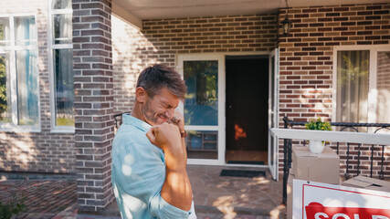 excited man with closed eyes near board with sold lettering and new house.