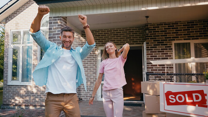 excited man rejoicing near wife, new house and sold board.