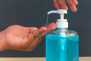 Hands pressing on a thin hand sanitizer on a wooden table. New normal and hygiene lifestyle concept.