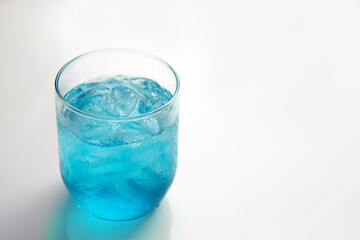 Closeup cold Blue Hawaii cocktail with ices in a clear glass on white isolated minimalism background with copy or negative space