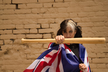 Pretty young girl with pigtails, heterochromia and punk style sucking a baseball bat with one hand and a UK flag rolled up in her body.