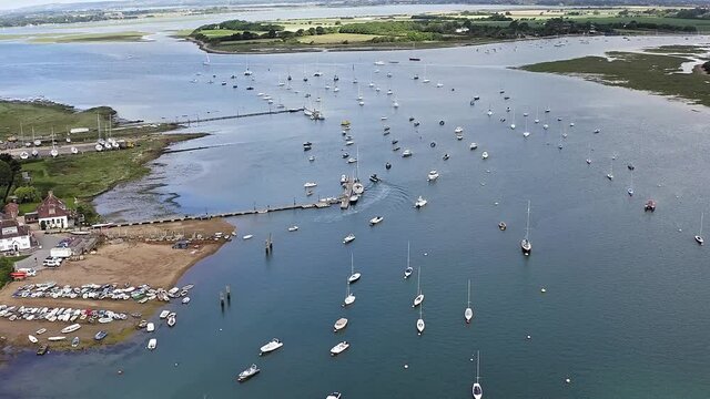 Aerial Footage along the beautiful estuary at Itchenor with boats and Yachts at anchor as a boat maneuverers by a jetty.