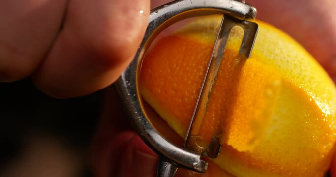 Male hands peeling orange fruit with special tool on black background. Close up shot in slow motion with RED camera.