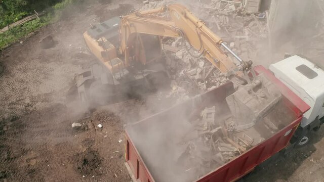 Demolition of building. Excavator loads construction waste into truck, aerial drone point of view.