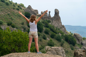 Woman raising hands up on top of mountain and looking to valley and peaks below. Healthy outdoors lifestyle concept