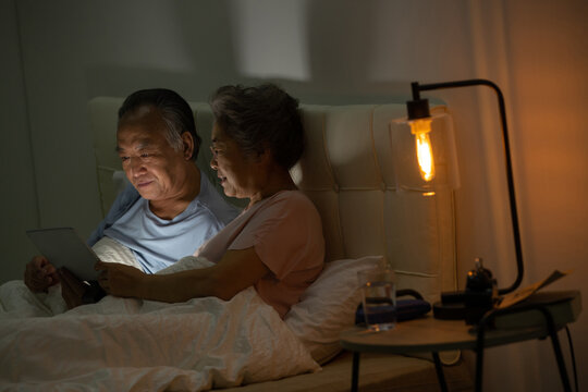 Elderly couple sitting on the bed see video with tablets
